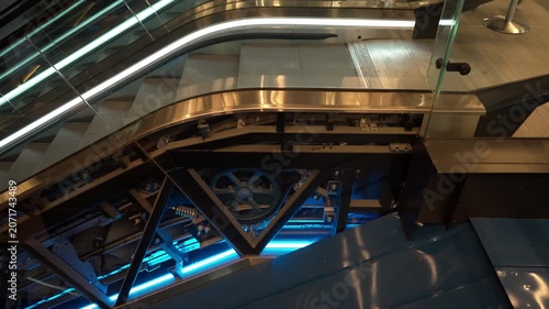Escalator mechanism operates inside public building. Exposed internal gears, chains and drive wheel show mechanical engineering, technical maintenance, machinery and urban infrastructure.