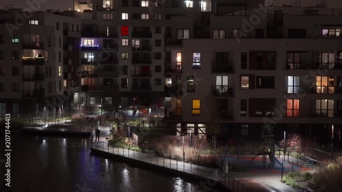 Residential apartment building complex illuminated at night stands in city district. Lit windows reveal urban housing estate property blocks within quiet neighborhood evening environment.