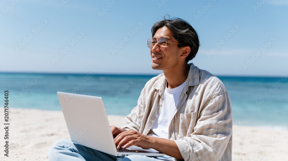 Fototapeta premium Young man working on laptop on a sunny beach with ocean background
