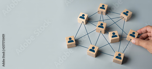 Hand connecting wooden cubes with people icons forming network structure.