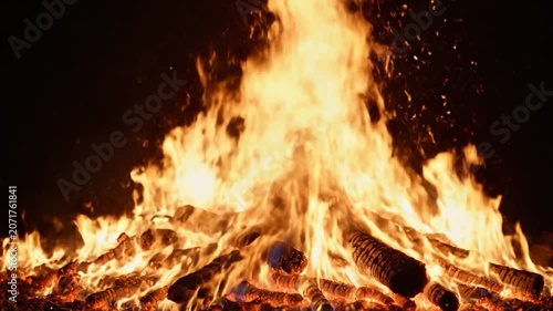 Bright orange flames burn intensely on a wooden campfire at night