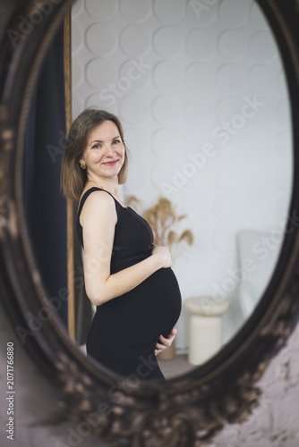 Reflection of a happy pregnant woman touch her belly in an ornate vintage mirror.