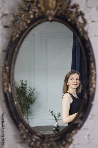 Reflection of beautiful smiling woman in a classic ornate vintage mirror.