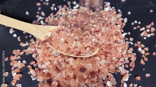 pink Himalayan salt falling in wooden spoon, highlighting its natural texture and color, perfect for culinary and wellness uses, slow motion