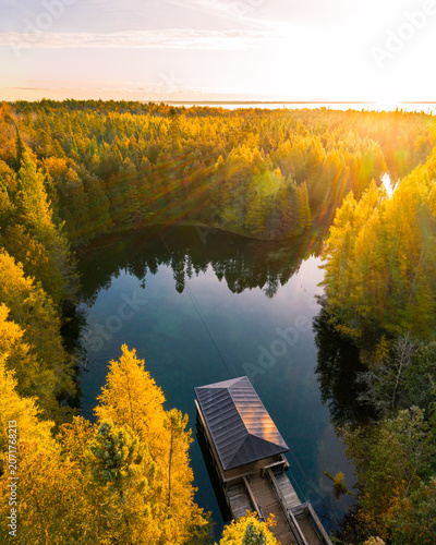 Aerial view of Kitch-iti-kipi, a natural spring with crystal clear water surrounded by dense autumn forest with golden foliage and a wooden observation raft, Michigan, United States.