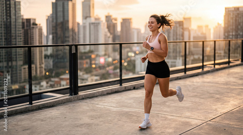 A fit young woman in athletic wear jogs along a rooftop terrace with a smartwatch as a glowing city skyline fades into sunset