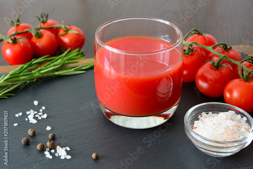 Glass of tomato juice with fresh tomatoes, rosemary, salt, and pepper close up
