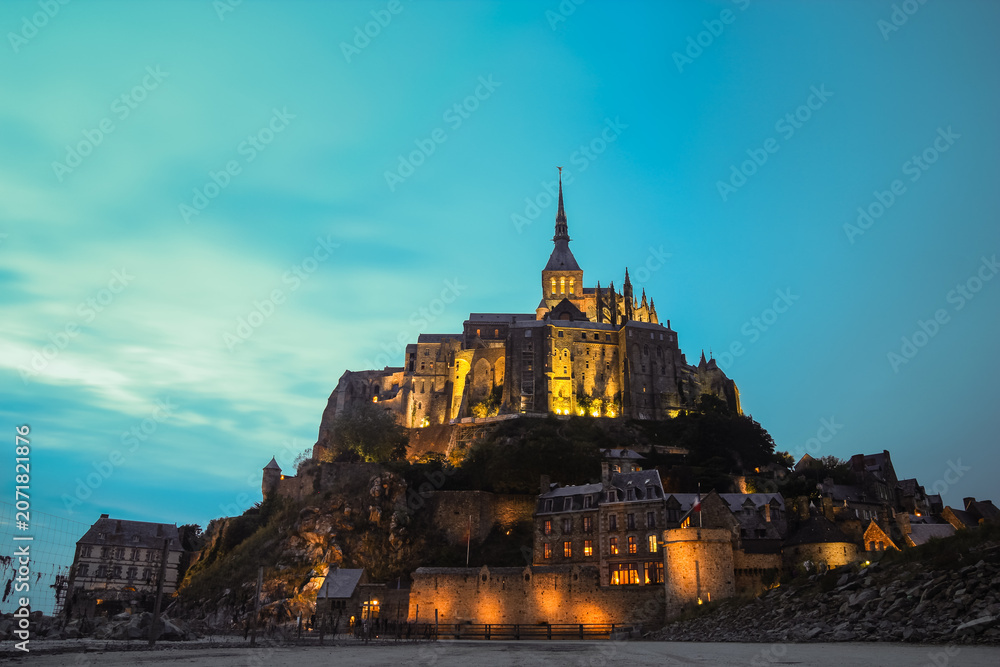 Naklejka premium Evening view of the historic tidal island of Mont Saint-Michel illuminated against a twilight sky in Normandy