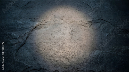Spotlight illuminating rough dark grey stone texture with natural cracks