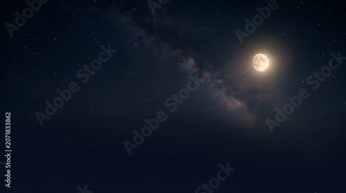 Bright full moon glowing in a dark night sky with the faint milky way galaxy