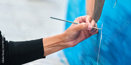 Bild auf Leinwand Close up of hand painting fine detail on bright blue canvas with brush outdoors