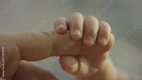 Close-up of a child's hand grasping an adult's finger, showcasing the tender connection and progression of touch in a soft, warm environment