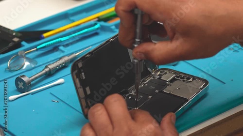Technician repairing smartphone motherboard after disassembly in electronics repair workshop