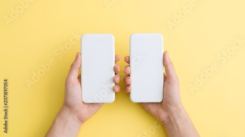 Hand Holding White Mobile Phones Against Yellow Background for Technology Concept