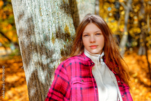 Young woman stands by a tree in a forest during autumn with colorful leaves on the ground