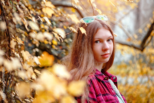 Girl stands near yellow leaves in a park during autumn afternoon light