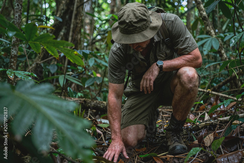 A forest ranger crouching on his knees, examining the ground for tracks left by animal poachers. Hunter hot on the trails of his prey. Officer searching for clues of missing person lost in the woods.