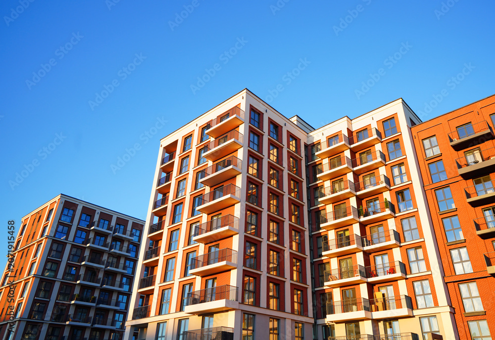 Fototapeta premium Facade of modern condominium in red and white colourful. Facade apartment building under blue sky. Modern facade building background. Balconies on blue sky. Modern residential facade 