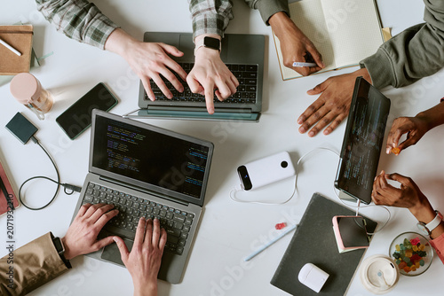 Tableau sur toile Overhead shot of diverse young adult team coding on laptops and tablet, sharing notes during software project collaboration