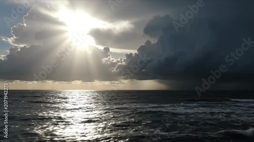 Dramatic sunbeams pierce through stormy clouds over a vast, shimmering ocean.