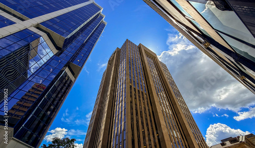 Tall buildings stand near each other under a bright blue sky with clouds
