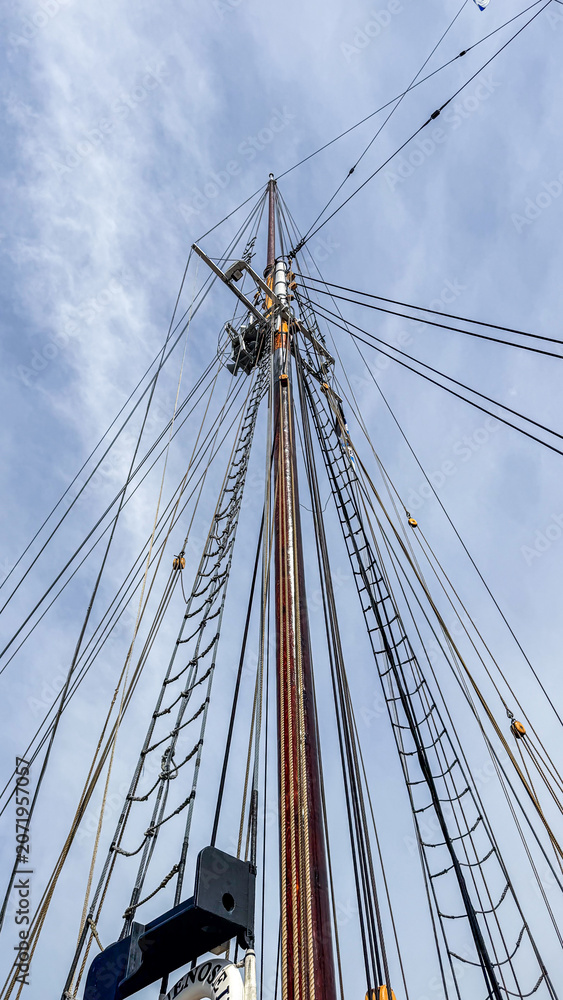 Obraz premium Tall ship mast with rigging reaching toward blue sky