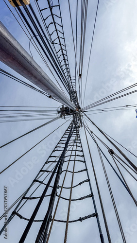 Looking up at the tall mast with many ropes on a sailing ship in the daytime