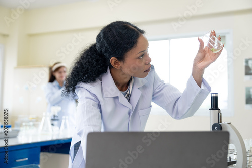 African American female scientist working with microscope and notebook computer in laboratory