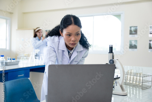 African American female scientist working with microscope and notebook computer in laboratory