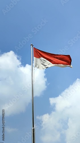 Red and white Indonesian flag waving on the top of the flag pole against blue sky and white clouds