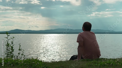 A lonely man sits on the shore of a lake and admires the beauty of nature, drawing inspiration and peace. Harmony of nature and man. Alone with myself.