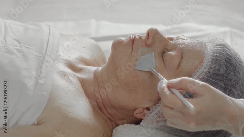 The process of applying an alginate mask to the face of an elderly woman in a beauty salon