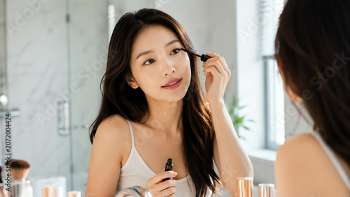 A woman applying mascara in a bright bathroom, showcasing a daily beauty routine with elegance and confidence.