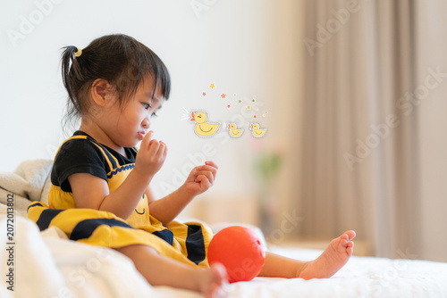 Cute Toddler Playing with Imagination and Cartoon Duck Illustrations on Bed at Home.