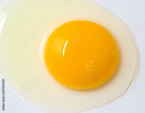 Cracked Fresh Chicken Egg with Golden Yolk Flowing on White Surface
