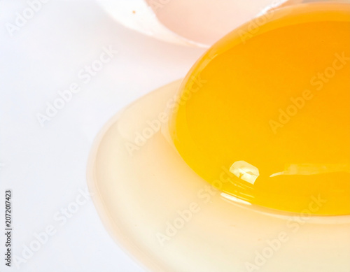 Cracked Fresh Chicken Egg with Golden Yolk Flowing on White Surface