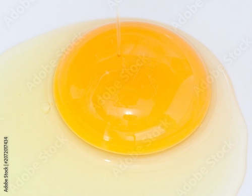 Cracked Fresh Chicken Egg with Golden Yolk Flowing on White Surface