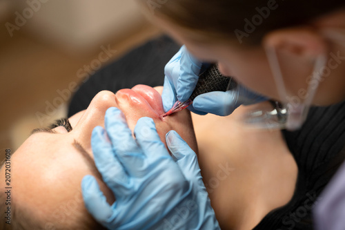 Принти на полотні Close up of beautician in blue gloves applying permanent makeup on female lips