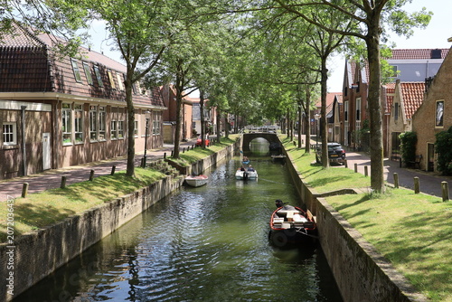Obraz na plátne A picturesque canal lined with green trees runs through the historic town of Medemblik in North Holland