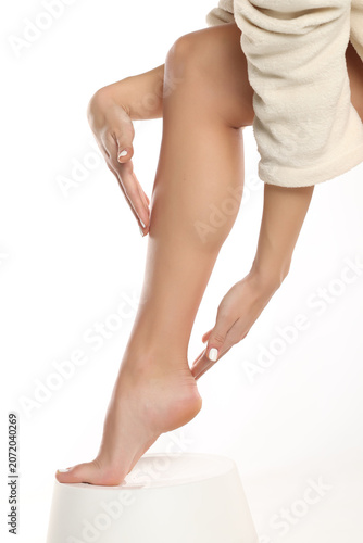 Studio shot of a woman’s leg and foot on tiptoes touching smooth depilated skin for body care and skincare on a white background