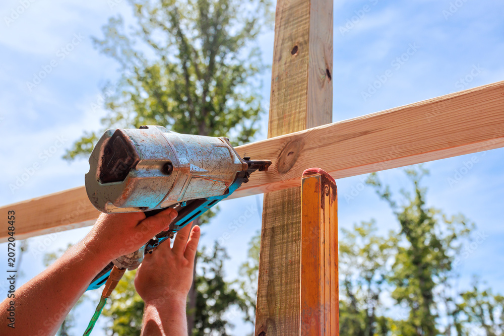 Obraz premium Builder operates air nail gun to secure wood beams at construction location