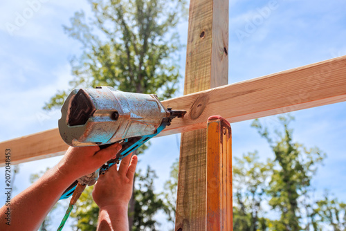Foto Builder operates air nail gun to secure wood beams at construction location