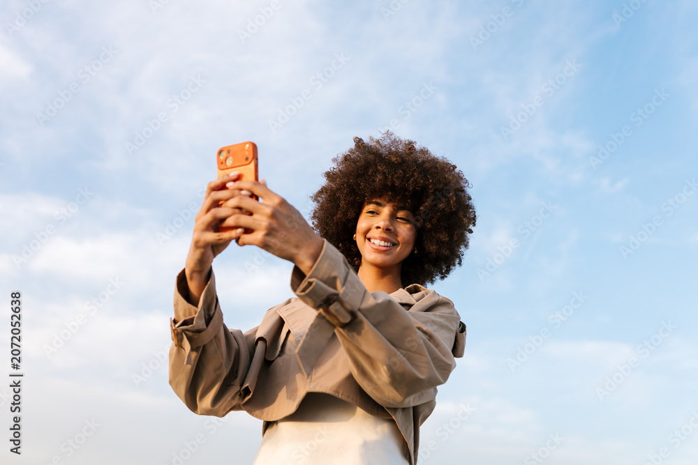 © Ezequiel Gimenez/Stocksy - Happy woman recording video on smartphone outdoors