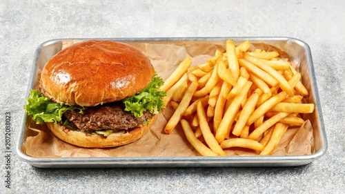 Juicy beef burger with lettuce and golden fries on a metal tray