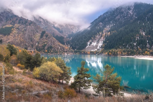 Turquoise Issyk lake surrounded by mountains and autumn forest in Almaty region, Kazakhstan. Scenic wilderness background for travel destination, nature conservation, or tourism commercial layout.