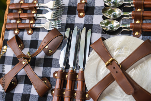 Canvastavla Polished forks, spoons, and serrated knives secure with tan leather straps and brass studs