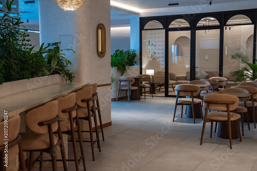 Tableau sur toile Softly lit lounge interior in the Maldives with tan leather barstools, white stone counter, rounded wooden chairs, arched glass partitions, plants, and pendant