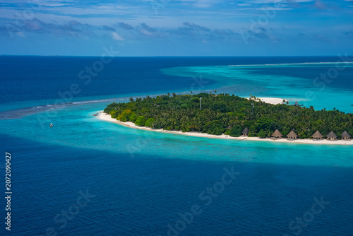 Tableau sur toile Aerial view of a Maldives atoll island in the Indian Ocean with palm forest, thatched beach villas, white sand, turquoise lagoons, and sweeping sandbars at midday