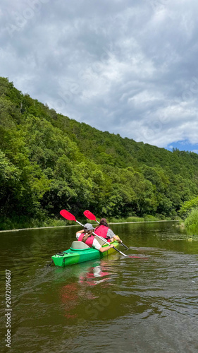 Kayaker paddling along a picturesque river surrounded by lush green forests and natural landscapes, calm water reflecting the sky and trees