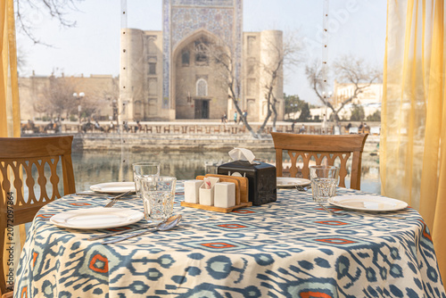 Set restaurant table with a traditional blue and white ikat pattern tablecloth, overlooking an old blurred madrasah onLyabi Hauz Square in Bukhara. Traditional regional textile design (ikat) 